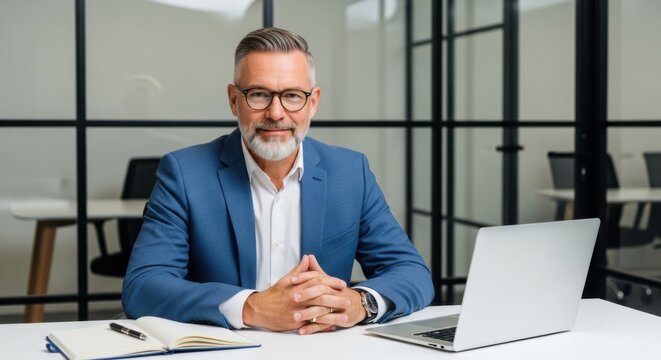 Mature businessman is sitting at his desk with a laptop - Powered by Adobe