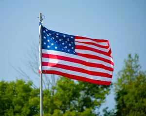 The American flag flies up a flagpole on a beautiful summer day with a background of blue sky and...