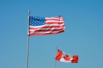 The American flag and Canadian flag fly together against a clear blue sky. 