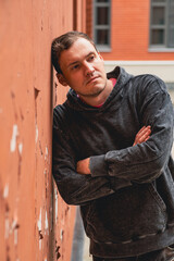 A young man is leaning against a textured orange wall in an urban area He appears deep in thought...
