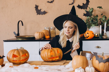 Woman wearing witch costume carving Halloween pumpkin at home