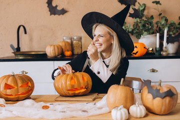 Smiling woman wearing witch costume carving Halloween pumpkins