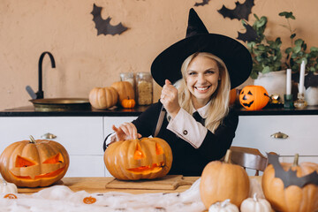 Smiling woman carving Halloween pumpkin wearing witch costume