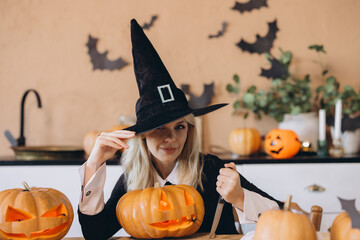 Woman wearing witch costume carving Halloween pumpkin with knife