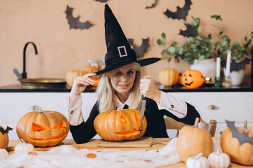 Young woman carving Halloween pumpkins wearing witch costume