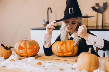 Woman wearing witch costume carving Halloween pumpkins