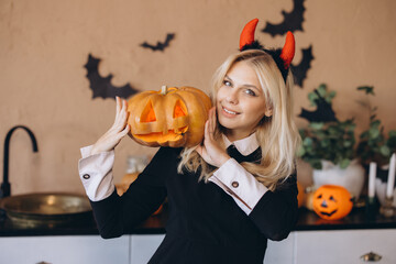 Smiling woman wearing devil horns holding jack o' lantern for Halloween party
