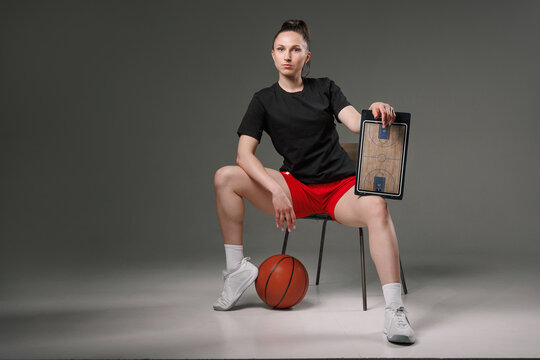 Female basketball coach with tactics board and ball teaching teamwork, strategy, and motivation in professional sports.