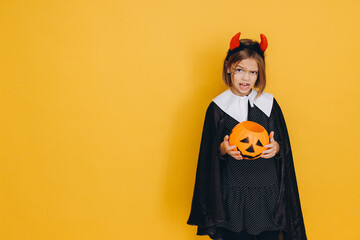 Little Girl Wearing Witch Costume Holding Pumpkin Basket on Yellow Background for Halloween