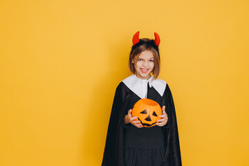 Little Girl Wearing Witch Costume Holding Pumpkin Basket for Halloween on Yellow Background