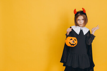 Little Girl Wearing Witch Costume Holding Pumpkin Basket on Yellow Background