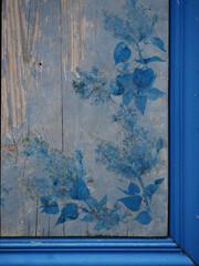 old window frame closed by wooden boards decorated with blue paint of flower ornaments