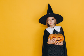 Little witch holding jack o' lantern posing on yellow background for Halloween