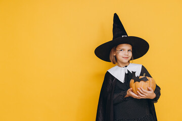Smiling girl wearing witch costume holding pumpkin for halloween party on yellow background
