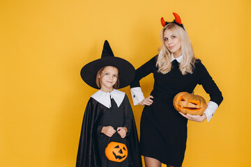 Mother and daughter wearing Halloween costumes holding pumpkins posing on yellow background