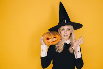 Halloween witch holding jack o' lantern with surprised expression on yellow background