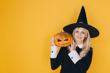 Smiling woman wearing witch costume holding jack o' lantern for halloween party