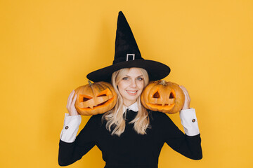 Smiling witch holding two jack o' lanterns on yellow background