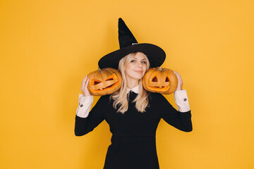 Smiling witch holding two jack o' lanterns on yellow background