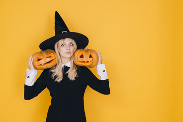 Woman wearing witch costume holding two jack o' lanterns on yellow background