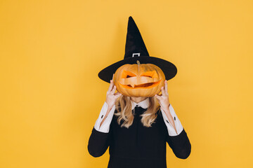 Young woman hiding face with halloween pumpkin wearing witch costume