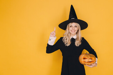 Smiling witch pointing up and holding jack o' lantern on yellow background