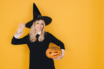 Smiling woman wearing witch costume holding carved pumpkin for Halloween party