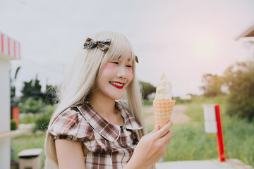 Young Woman with Long Blonde Hair Enjoying a Delicious Ice Cream Cone Outdoors During a Bright and...