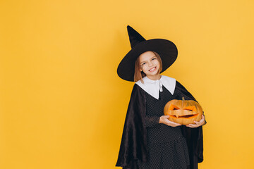 Smiling girl wearing witch costume holding jack o' lantern for Halloween party on yellow background