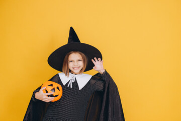 Little witch holding pumpkin basket posing on yellow background