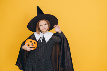 Smiling girl wearing witch costume holding pumpkin for Halloween posing on yellow background
