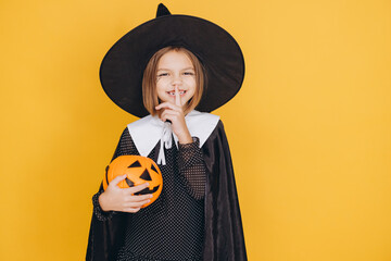 Little Witch Holding a Pumpkin Keeping a Secret on Yellow Background
