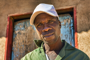 africa village, african smiling single man with a cap, in front of the house in the yard, blue door,