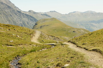 Chemin de randonnée traversant les reliefs verdoyants avec vue sur les sommets alpins
