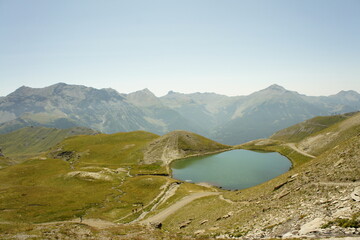 Lac de montagne entouré de reliefs verdoyants avec sommets alpins en arrière-plan