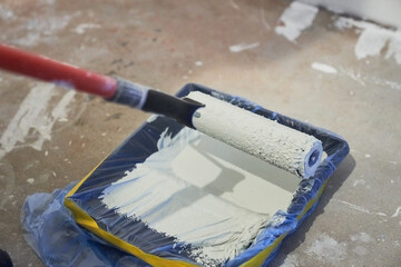 Apartment renovation. Concrete walls are painted gray with a paint roller. A container of paint for a paint roller. High quality photo