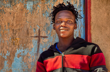 africa village, african smiling single young man with dreadlocks braids , in front of the house in...
