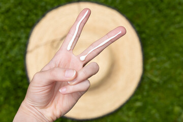 A person applying the correct amount of sunscreen for the face and neck &ndash; two finger lengths, with a straw hat in the background. Concept of applying sunscreen in summer. 