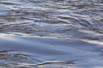 Close-up view of a flowing river surface with soft waves and sunlight reflections, ideal for nature...