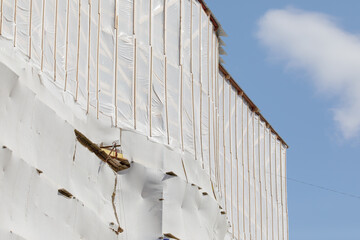 A construction worker stands on scaffolding, working on the side of a building covered in...