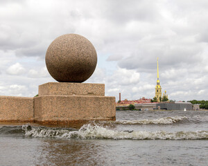 Stormy winds cause Neva River waters to rise and flood the embankment on Vasilyevsky Island, with waves splashing near the granite sphere and Peter and Paul Fortress in the background.