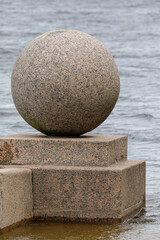 Close-up of a granite sphere sculpture on the Vasilyevsky Island embankment, partially surrounded by storm-swollen Neva River water.