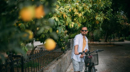 A young man with a bicycle on a green street with private houses. Eco-friendly transport.  Green...