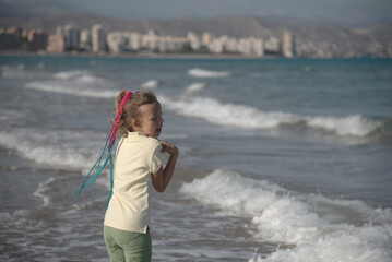 Child with Braids Looking at Ocean Waves. A young girl with colorful braided hair stands in the...