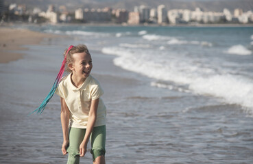 Child with Braids Looking at Ocean Waves. A young girl with colorful braided hair stands in the...
