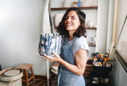 Latin ceramic artist holding painted vase in pottery studio, proud of handmade art and cultural identity