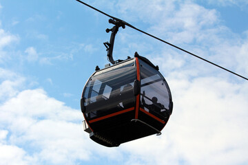 A sleek, glass-enclosed cable car gondola with black and orange accents glides along a cable high...