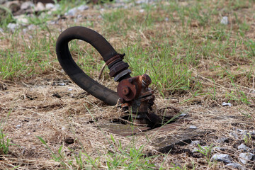 A corroded, rusted hydrant with a thick, flexible black hose protrudes from the earth in a patchy...