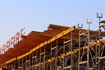 A network of metal scaffolding supports bright yellow wooden beams, forming the framework for a...