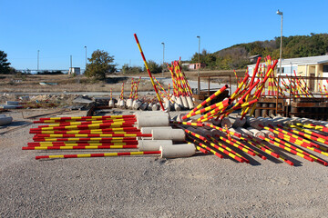 Numerous red and yellow striped concrete barriers and poles are stacked and scattered in an open...